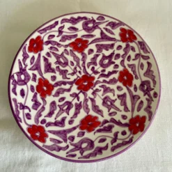 Assiette en céramique artisanale avec motifs floraux rouges et violets, fabriquée à la main par des artisans marocains