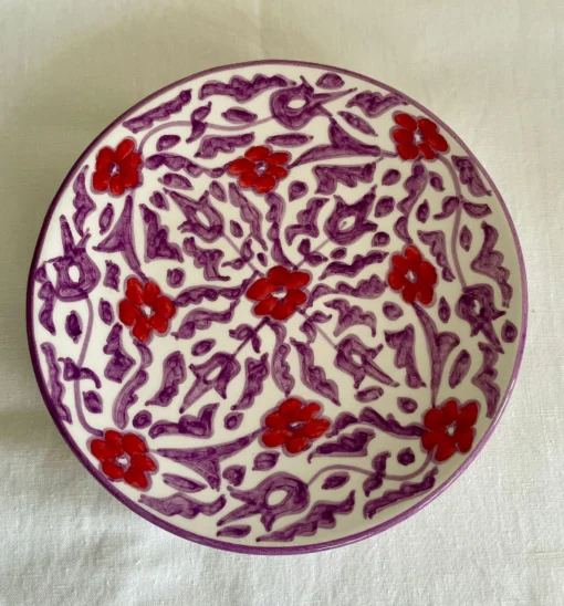 Assiette en céramique artisanale avec motifs floraux rouges et violets, fabriquée à la main par des artisans marocains